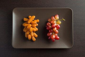 Arabic sweet Balah and bunch of fresh red grapes placed side by side on dark plate. Concept for healthy eating during Iftar. View from top. 