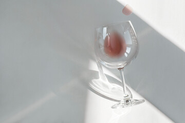 Tipped over wine glass with a little rose at the bottom, sun and shadows on the table