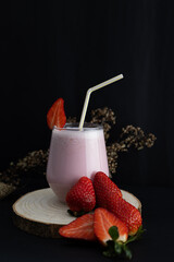 Vertical image of strawberry smoothie in a glass cup next to scattered strawberries on a rustic...