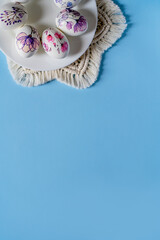 Easter beautiful decorated orthodox religious chicken eggs with flowers lie on a white porcelain plate on a blue background with a macrome napkin