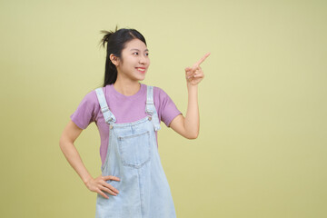 Young woman in casual outfit pointing and smiling against a light green background during a...