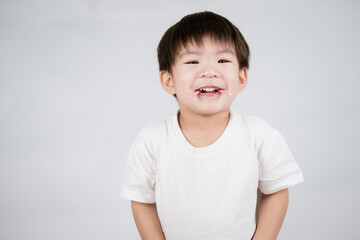 joyful child with messy face smiles widely, wearing white shirt against plain background. image captures moment of happiness and innocence, highlighting carefree nature of childhood