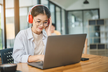 Student using a laptop in a cafe while wearing headphones, learning and searching the internet, and...