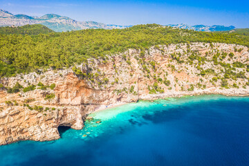 A breathtaking aerial view of Pasjaca Beach in Croatia, showcasing its secluded location beneath towering cliffs, golden sand, and the crystal-clear turquoise waters of the Adriatic Sea