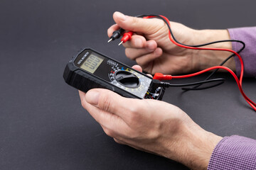 Hand holding a digital multimeter with test leads, on a dark background