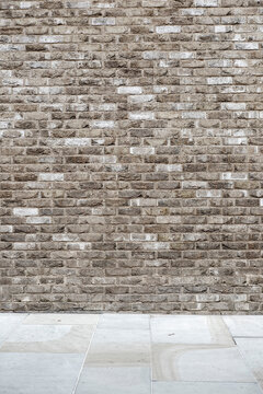 Fototapeta Textured brick wall with a clean urban pavement foreground.