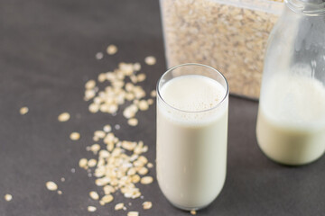 A glass of oat milk and oatmeal in a box on grey kitchen table. Vegan and non-dairy alternative milk
