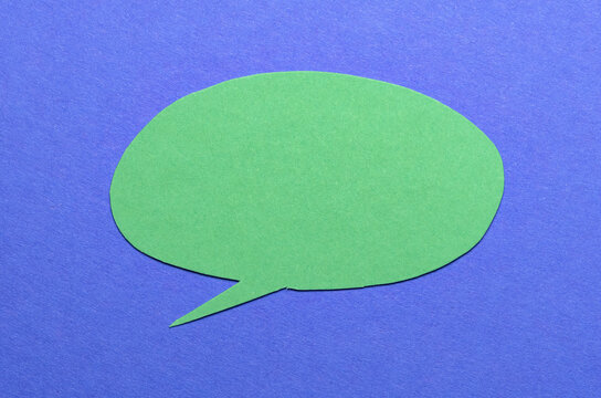 Green cut out blank paper speech bubble of round shape with copy space for text on blue background, flat lay top view conceptual backdrop