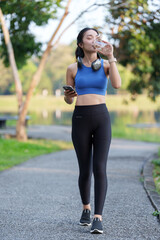 Active young woman enjoying a refreshing drink during a morning workout in a serene park setting,...