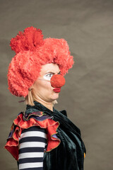 A woman in a clown costume with a red nose and red wig. She is smiling and looking at the camera