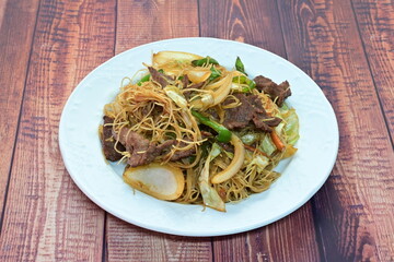 A plate of beef and vegetables with noodles on a wooden table
