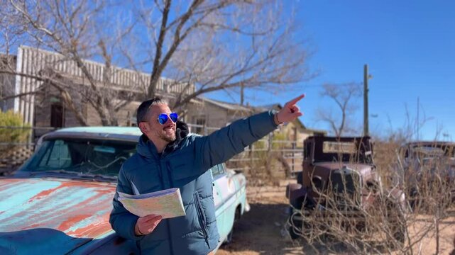 Tourist holding wrinkled map while searching for direction near classic vintage car parked alongside iconic Route 66 highway stretching through southwestern desert landscape