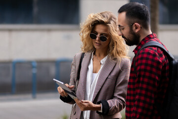 Professional woman and man discussing business using a tablet outdoors in an urban setting, both focused and engaged in their conversation, highlighting collaboration