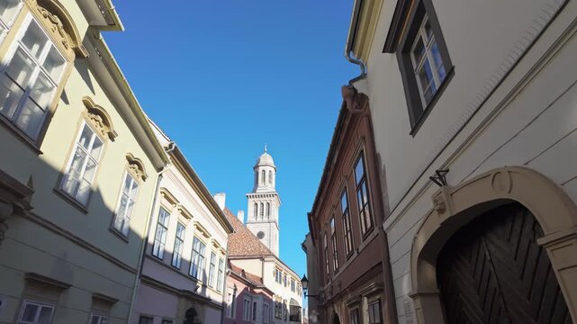 Walk in the historic old town of Sopron, where the tower of the Evangelical Parish Church rises above the classical houses with blue sky background in Hungary.
