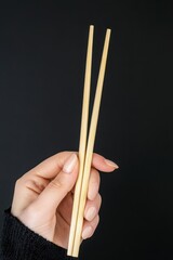 Woman's Hand Holding Light Beige Patterned Chopsticks Against Dark Background
