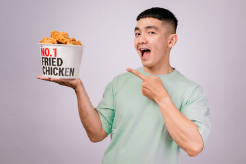 An Asian man in a light green shirt excitedly points at a bucket of fried chicken labeled 