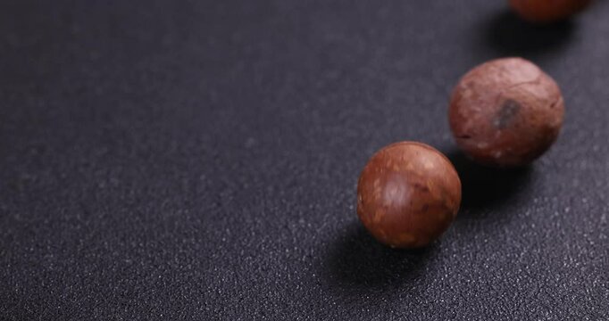 Macadamia nuts rolling on dark background