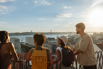 Tourists admiring lisbon skyline with 25th of april bridge at sunset from famous viewpoint