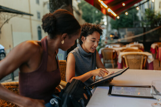 Two young women using tablet and consulting menu at restaurant