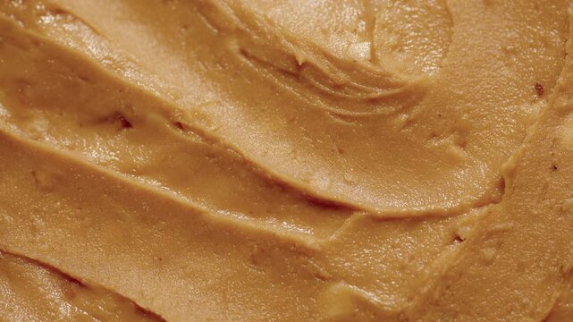 Peanut butter texture circle rotation close up top view. Crunchy peanut butter with peanut pieces. Classic peanut butter.