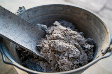 Iron bucket with a scoop filled with ash after cleaning the fireplace, close-up. Organic fertilizer for the garden