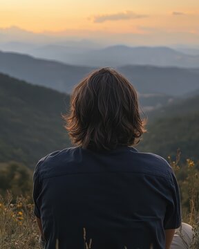 Man with straight, shoulder-length hair sitting on a mountain hill