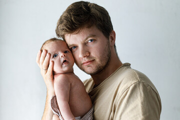 Fototapeta premium Happy Fathers day! Stylish father hugging cute little baby son close up against white wall. Fatherhood and parenthood. Adoption and fertility concept