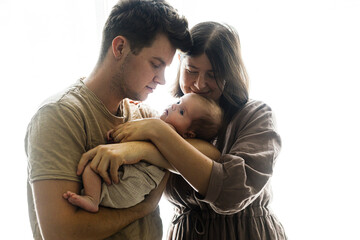Happy Mothers day and Happy Fathers day! Happy couple hugging little baby son in window light. Motherhood and parenthood. Adoption and fertility concept