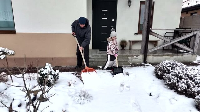 Happy dad and daughter clearing snow near house in winter outside