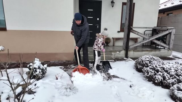 Happy dad and daughter clearing snow near house in winter outside