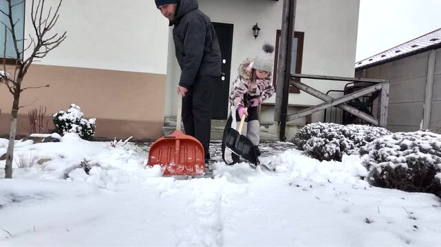 Happy dad and daughter clearing snow near house in winter outside