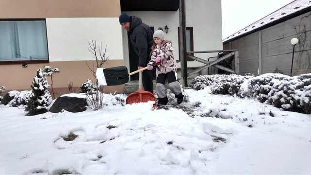 Happy dad and daughter clearing snow near house in winter outside