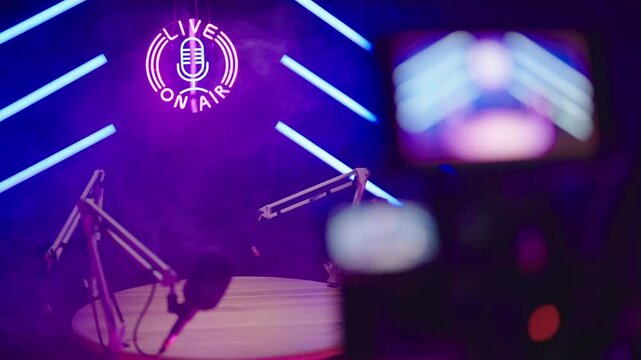 Behind the camera monitor refocus to podcast set in black studio with neon light