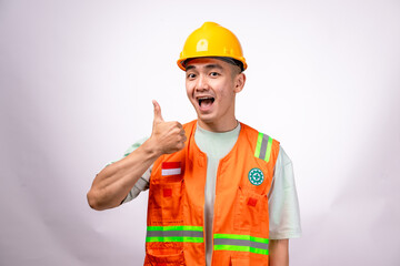 An Asian male construction worker wearing an orange safety vest and a yellow hard hat gives a...