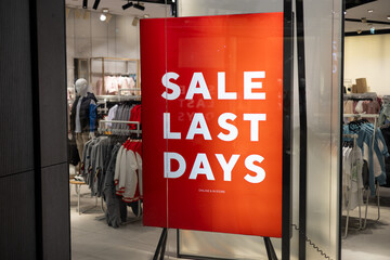 Sale sign in front of the clothing store. Sale last days. Red bright sale banner on window store. Discount information at store entrance, shopping season promotion