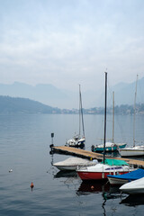 Fototapeta premium Tranquil lakeside marina with moored sailboats, calm water reflections and misty mountain backdrop creating a peaceful nautical atmosphere