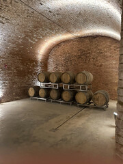 A wine cellar with stacked wooden barrels under a vaulted brick ceiling.