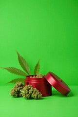 Green background with a red football-shaped cannabis grinder and dried leaves, green, branch