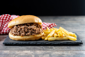 Traditional sloppy joe sandwich with french fries on wooden table and black background. Copy space