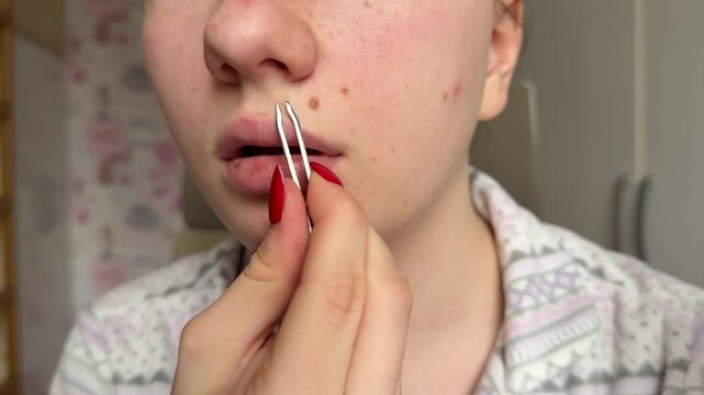 Young Woman Plucking Moustache Removing Hair Above Upper Lip Using Tweezers Looking Aside And Smiling Standing In Modern Bathroom At Home. Female Beauty Care Routine Concept