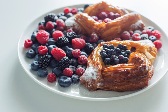 Danish with raspberries and blueberries on  round plate with berries on  white table