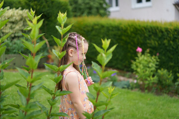 A sad, lonely, little cute girl in a dress with colorful small braids and a missing front tooth in...