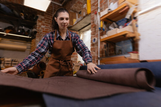 Portrait young woman craftsman tailor working with brown rolls of natural color leather on atelier workshop - Powered by Adobe