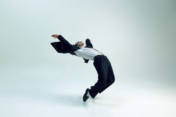 Young businessman arching backward with flowing jacket and open posture against white studio...