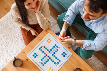 Couple enjoying spending leisure time together at home playing ludo board game