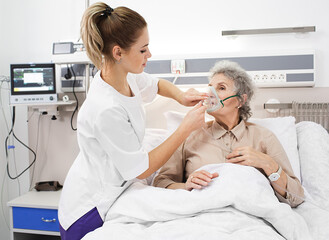 Healthcare worker supporting an elderly patient by fitting a breathing mask for respiratory care in a well-equipped medical clinic