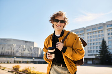 Stylish young man enjoys coffee while walking in the sunny city square during afternoon hours