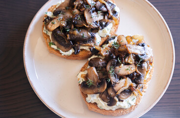 delicious mushroom toast with herb cream cheese, mushrooms, and caramelized onions on a white modern plate close-up
