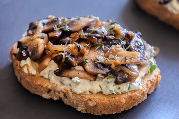 delicious mushroom toast with herb cream cheese, mushrooms, and caramelized onions on a black stone plate close-up