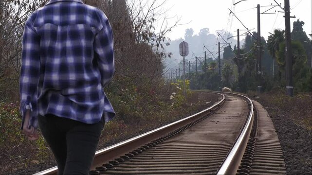 A young female traveler walking on railway tracks surrounded by nature. Tourism, freedom, and peace, walking along the rails in the greenery.Traveler on the railway tracks. solitude, adventure,harmony